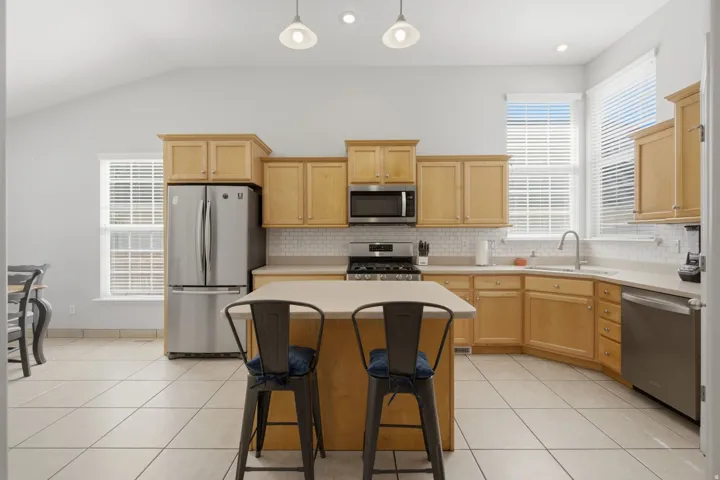 Kitchen featuring light wood cabinetry, stainless steel appliances, a center island, tile flooring, and vaulted ceilings