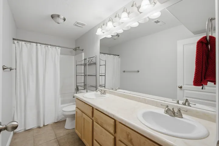Double vanity with undermount sinks and brushed nickel faucets, light wood-finish cabinetry, full-width mirror, and ceramic tile flooring