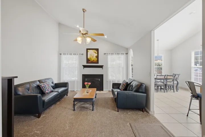 Vaulted ceiling with ceiling fan, fireplace with mantel, arched window, and recessed lighting