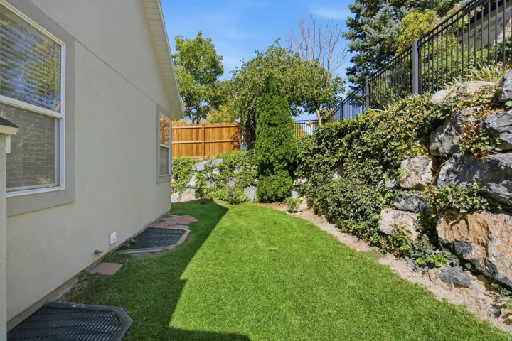 Manicured lawn area with a rock retaining wall, mature trees, and a privacy fence