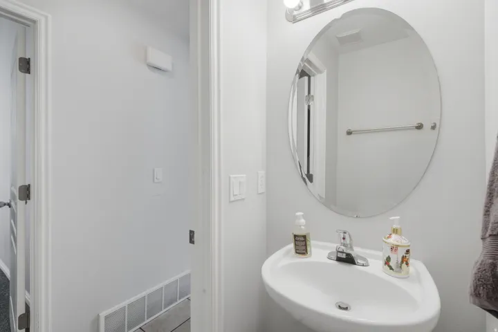 Wall-mounted sink with chrome faucet, complemented by an oval mirror and overhead vanity lighting
