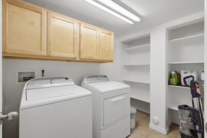 Laundry area featuring light wood-finish cabinetry, built-in shelving, tile flooring, and overhead strip lighting