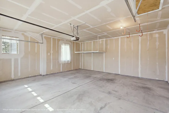 Concrete flooring in a spacious garage with exposed drywall, overhead storage, and an attached garage door opener