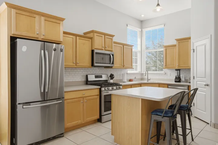 Kitchen featuring wood cabinetry, stainless steel appliances, white subway tile backsplash, and an island with countertop seating