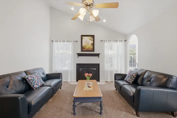 Vaulted ceiling with recessed lighting and a ceiling fan, arched window, fireplace with a decorative mantel, and carpet flooring