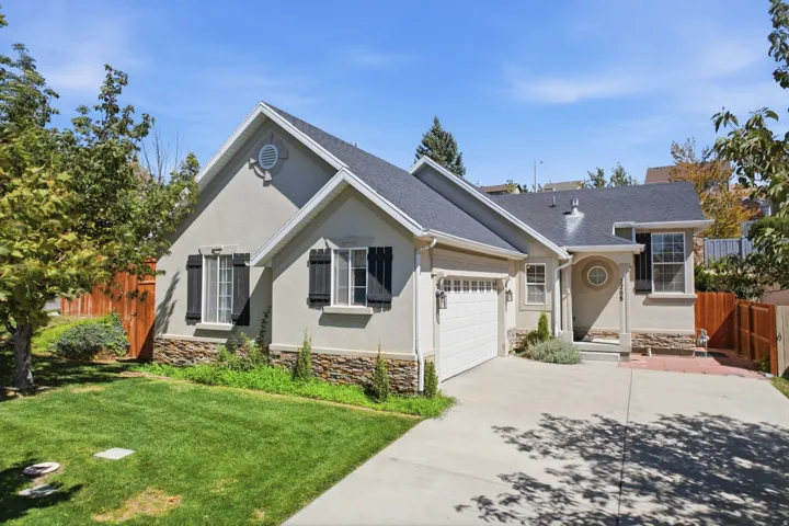 Stucco exterior with stone accenting, black framed shutters, attached garage, and a concrete driveway