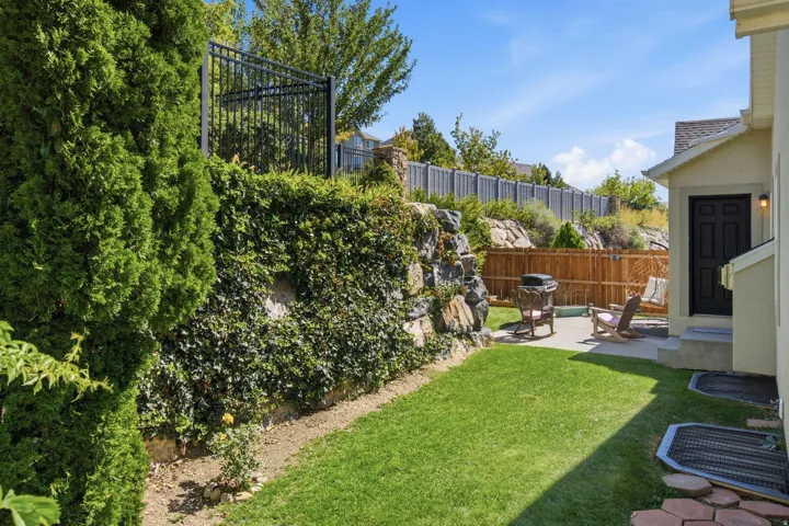 Manicured lawn with a concrete patio, retaining wall with climbing ivy, and a privacy fence