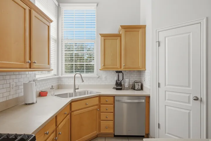 Kitchen featuring light wood cabinetry, a stainless steel dishwasher, a single basin stainless steel sink, and a white subway tile backsplash
