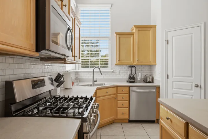 Kitchen featuring wood cabinetry, stainless steel appliances, tile backsplash, and light-toned countertops