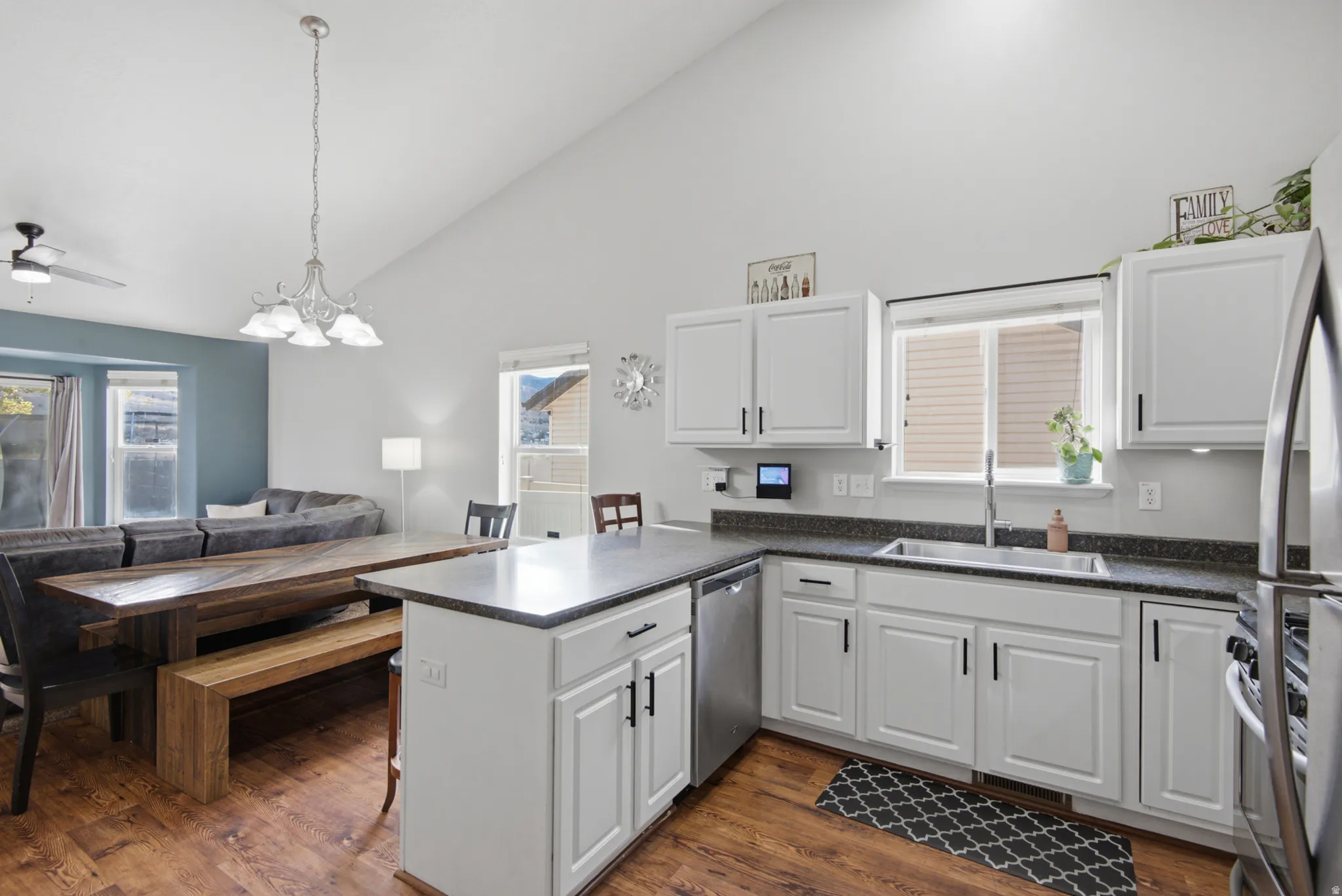 Vaulted ceiling, wood-finish flooring, white cabinetry, dark countertops, and stainless steel appliances