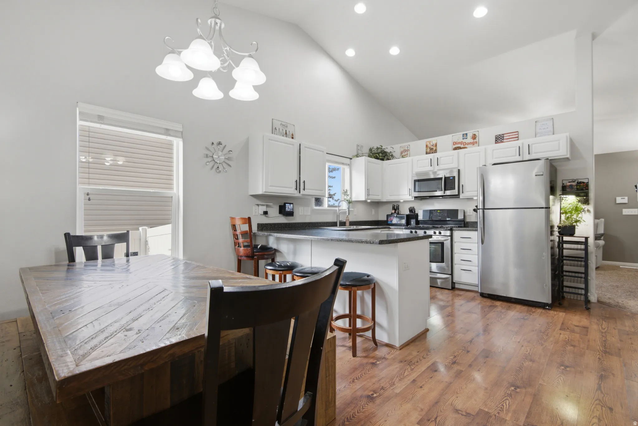 Vaulted ceiling, recessed lighting, wood-finish flooring, white cabinetry, and stainless steel appliances