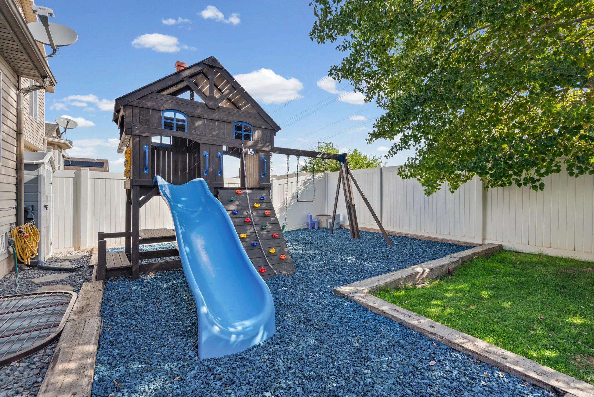 Outdoor play structure with a blue slide, rock climbing wall, and swing set