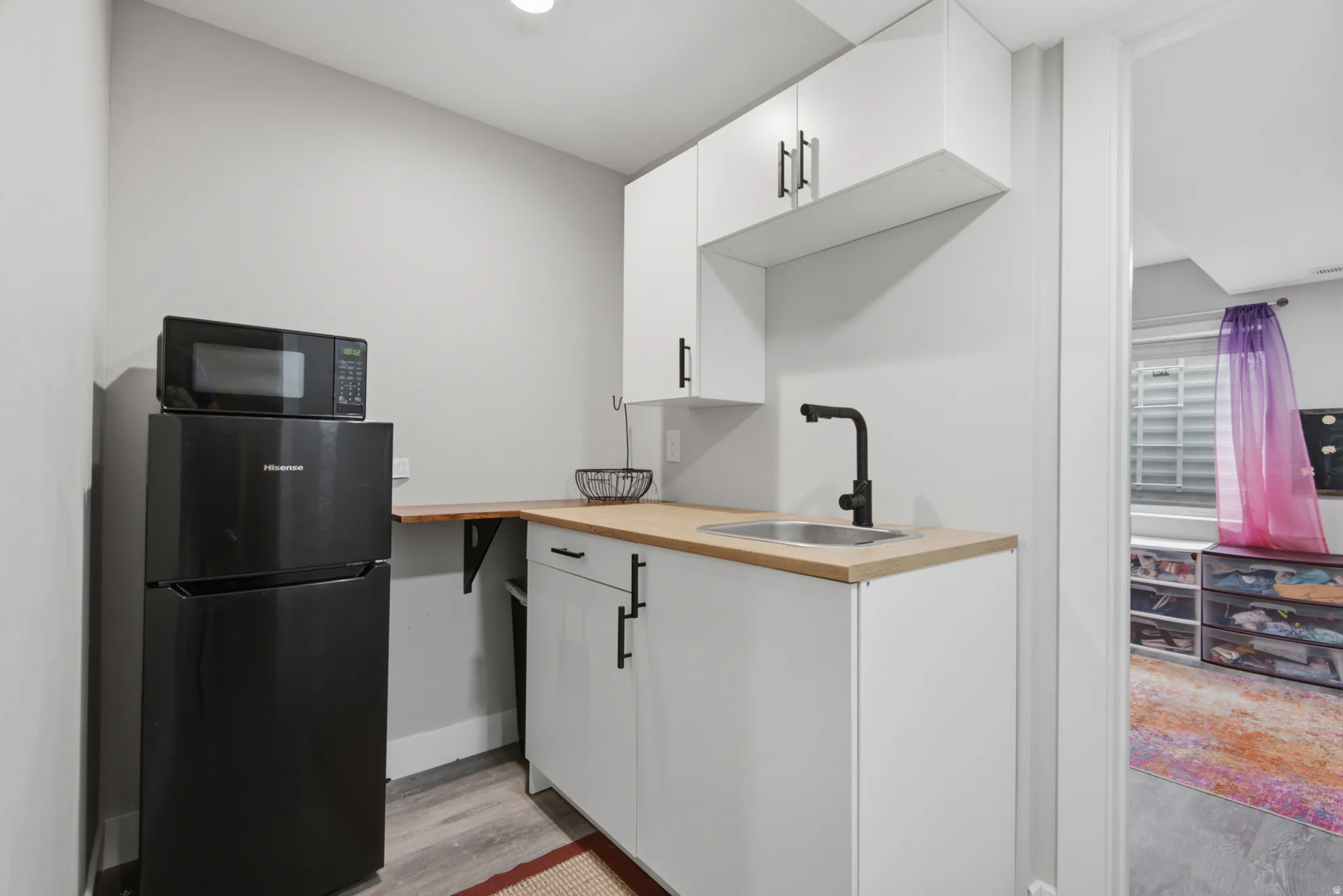 Compact kitchen area featuring white cabinetry, light wood-finish countertops, and a stainless steel sink with a matte black faucet