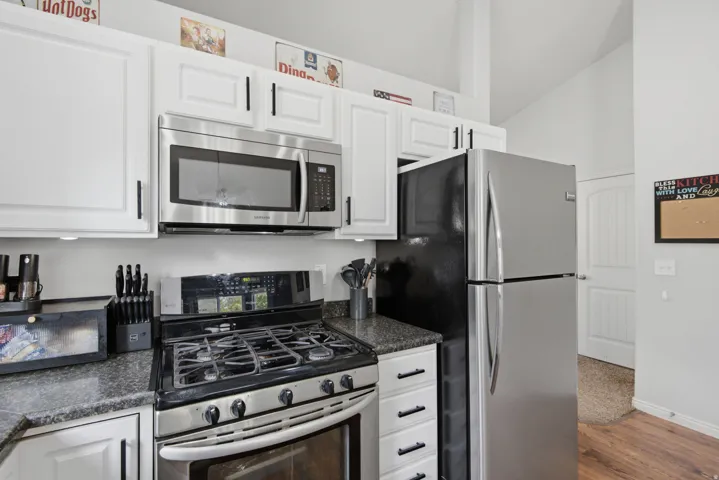 White cabinetry with black hardware, stainless steel appliances, dark granite countertops, and a vaulted ceiling