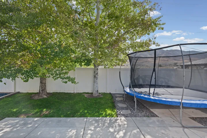 Manicured lawn with mature trees, white privacy fencing, and concrete patio