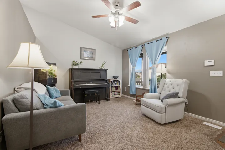 Vaulted ceiling with a ceiling fan, dual windows with curtain rods, and carpet flooring