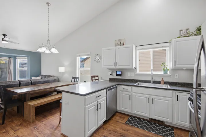 Vaulted ceiling, wood-finish flooring, white cabinetry, dark countertops, and stainless steel appliances