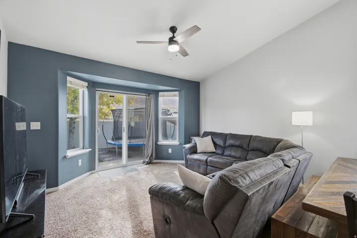 Carpeted room featuring a ceiling fan with integrated lighting, a sliding glass door, and multiple windows