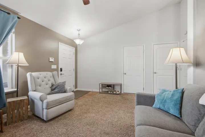 Vaulted ceiling with ceiling fan, wall-mounted light fixture, white interior doors, and textured carpeting
