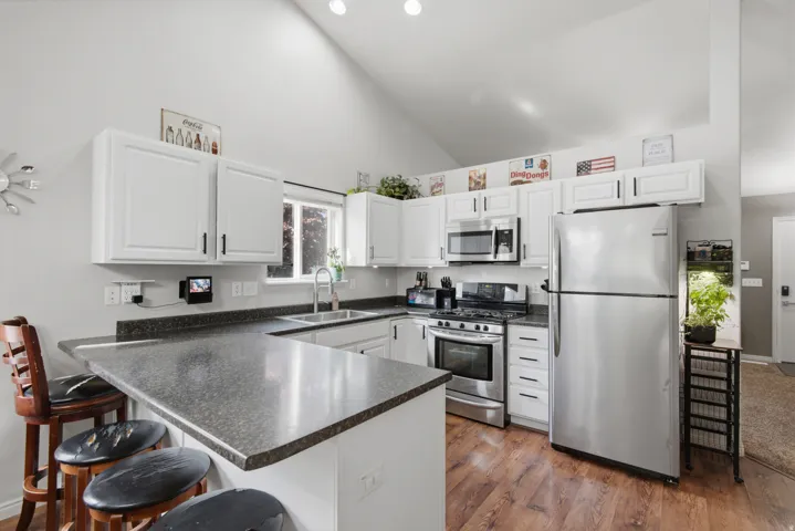 Kitchen featuring white cabinetry, stainless steel appliances, dark countertops, wood-finish flooring, and vaulted ceilings