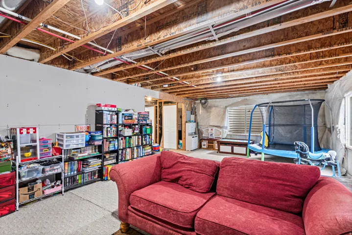 Unfinished basement with exposed ceiling joists and support beams, featuring partial drywall installation and an exposed window opening