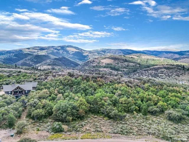 Expansive mountain landscape with diverse foliage, featuring a multi-level residence with a covered balcony