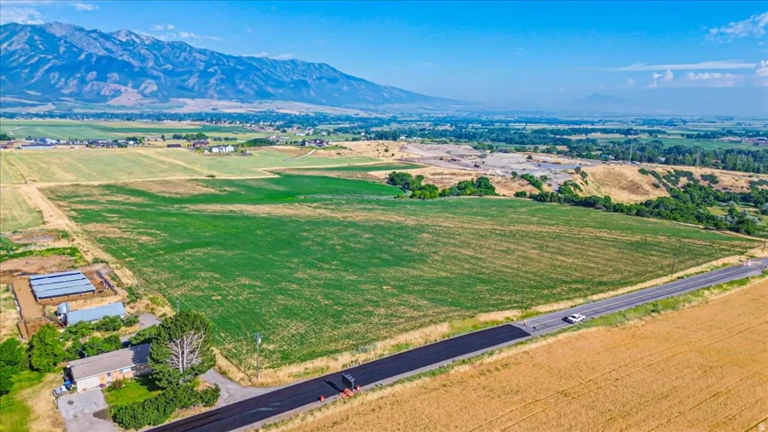 Expansive land parcel featuring agricultural fields, a paved roadway, and distant mountain ranges