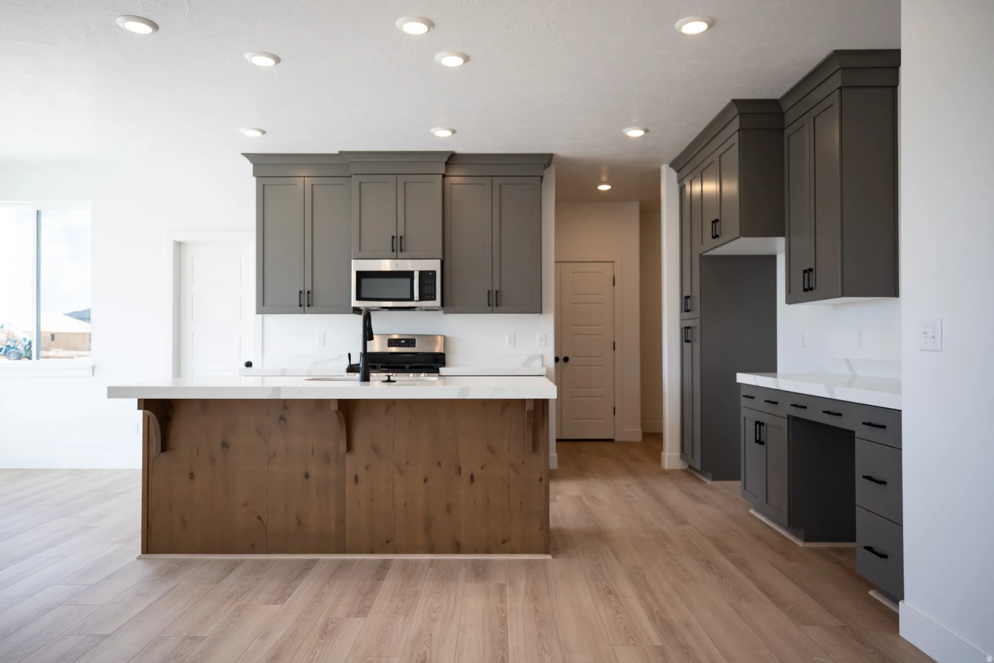 Terrific kitchen with ceiling-height uppers, painted wood cabinets, stained wood island, quartz slab countertops, built-in desk, gas range, microwave, dishwasher and disposal.