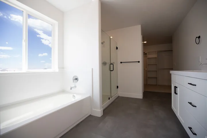 Primary bath with dual sinks, painted white wood cabinets, quartz slab countertops, soaker tub and walk-in Euro shower.