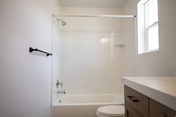 Full secondary bath with stained wood cabinet, extra-long vanity and quartz slab countertops.