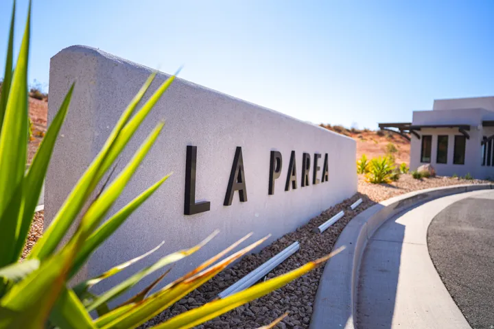 Property entrance featuring a concrete sign with raised lettering, landscaped with gravel and desert plantings