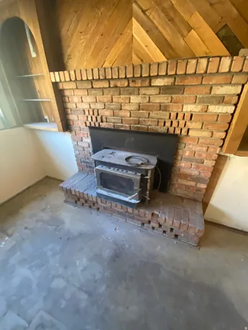 Brick fireplace with a wood-burning stove insert, herringbone wood accent wall, built-in shelving, and a brick hearth