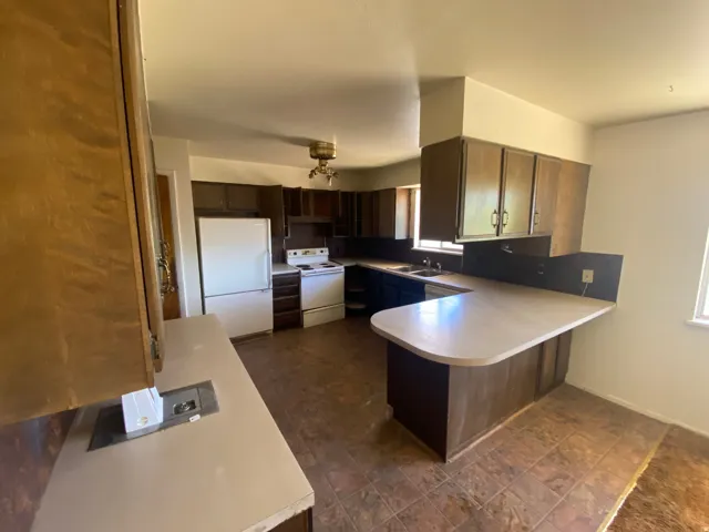 Kitchen featuring dark wood cabinetry, white appliances, a double basin sink, and a peninsula with seating space