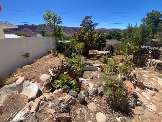 Landscaped hillside featuring a white privacy fence, mature trees, and natural rock elements