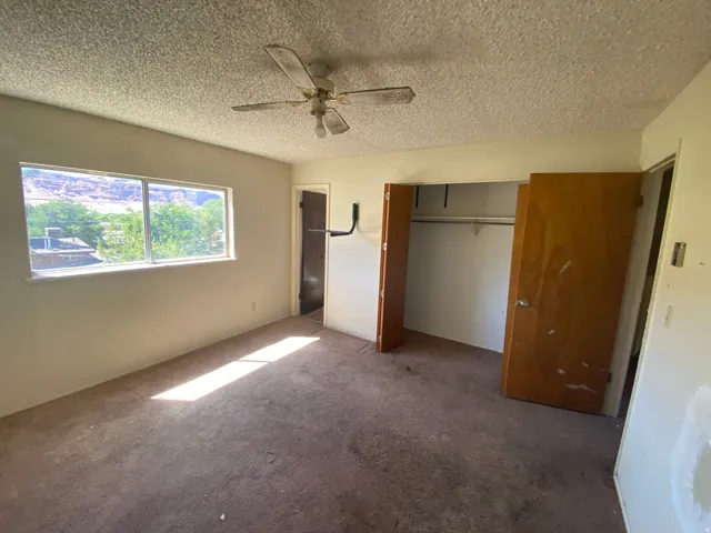 Carpeted room featuring a ceiling fan, a window, and a built-in closet with bi-fold doors