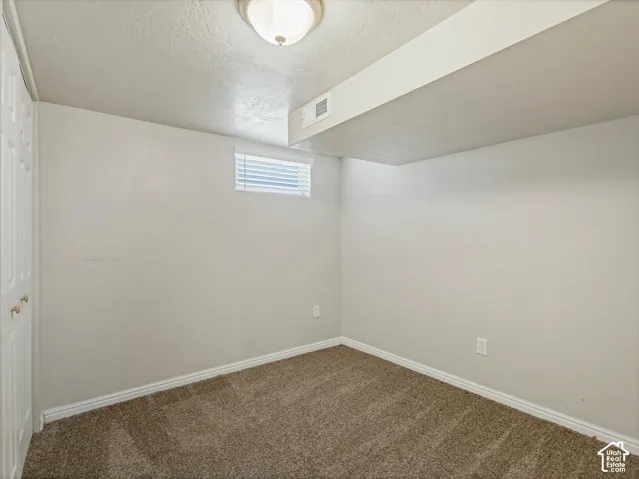 Recessed window with blinds, overhead flush mount light fixture, textured ceiling, light neutral wall paint, and brown carpeting