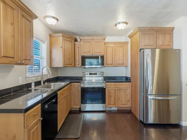 Wood-finish cabinetry, stainless steel appliances, dark countertops, dark wood-finish flooring, and recessed lighting