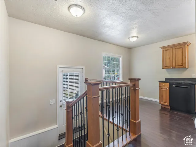 Hardwood flooring, wood newel posts, wrought iron balusters, wood cabinetry, and a built-in black dishwasher