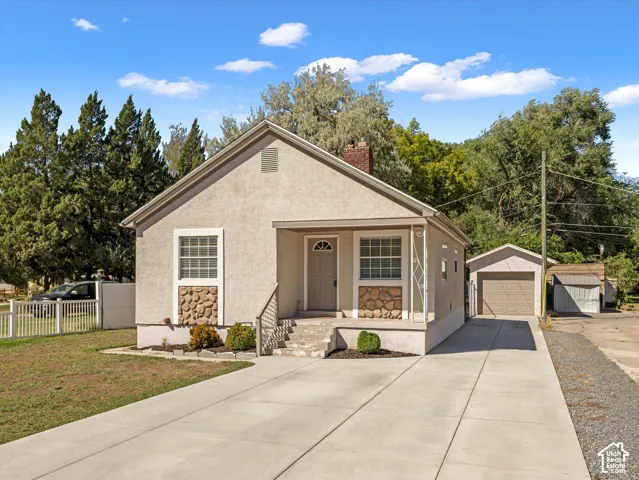 Stucco exterior with stone accents, covered front entry, concrete driveway, detached garage, and white picket fencing