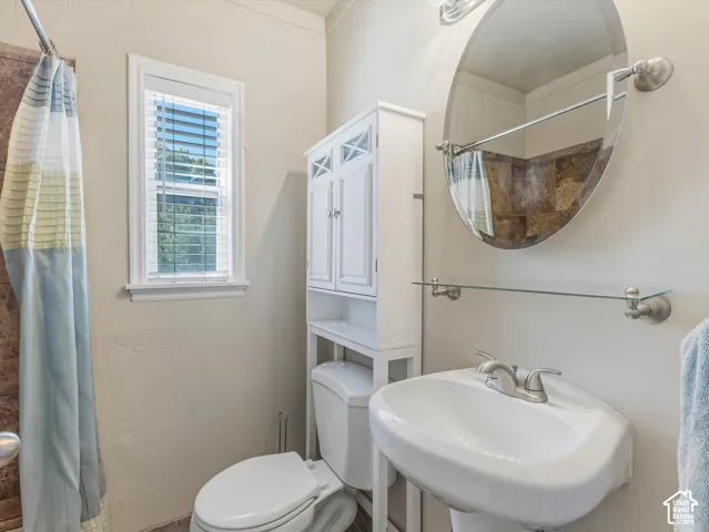 Bathroom featuring a white pedestal sink, oval mirror, wall-mounted glass shelf, and a window with blinds