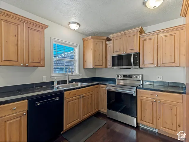 Hardwood-style flooring, stainless steel range, stainless steel microwave, black dishwasher, and wood cabinetry
