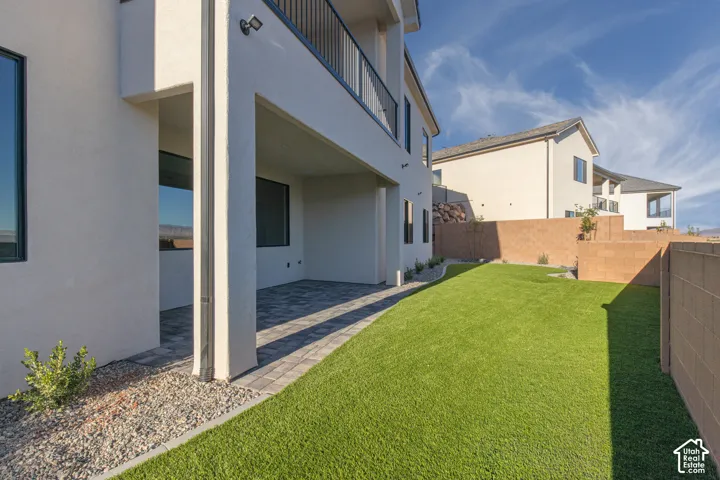 Expansive synthetic lawn with a paved patio, elevated block wall, and integrated exterior lighting