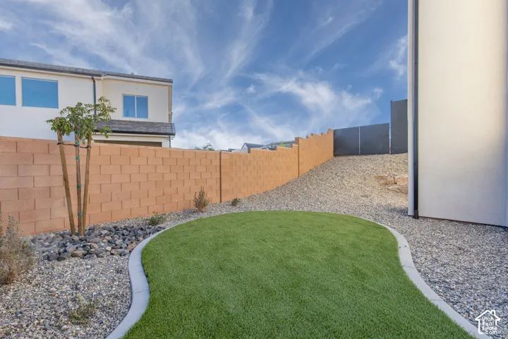 Curved artificial turf lawn bordered by gravel, featuring a block privacy fence and a small tree