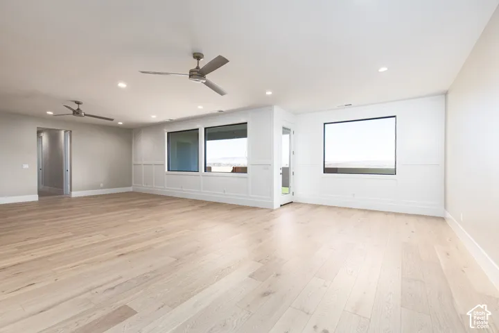 Spacious room featuring light wood-finish flooring, recessed lighting, and two ceiling fans