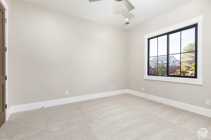 Bright, light-filled bedroom showcasing neutral carpet flooring, clean white walls with chair rail molding, and a large multi-pane window framing natural outdoor scenery