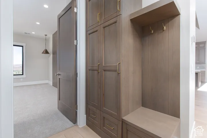 Sophisticated mudroom and entryway featuring custom wood-finish cabinetry with multiple storage cubbies, recessed ceiling lighting, neutral tile flooring, and an open shelving alcove with hooks for outerwear and accessories