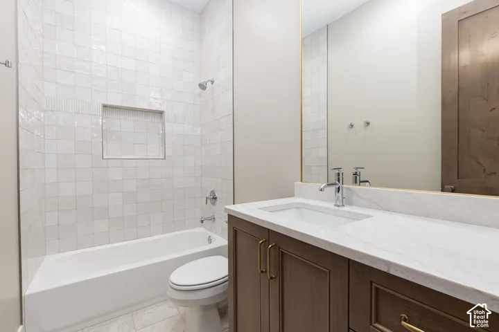 White tiled shower and tub combination with an integrated niche, wood-finish vanity with gold-tone hardware, white countertop with an integrated sink, and an expansive vanity mirror