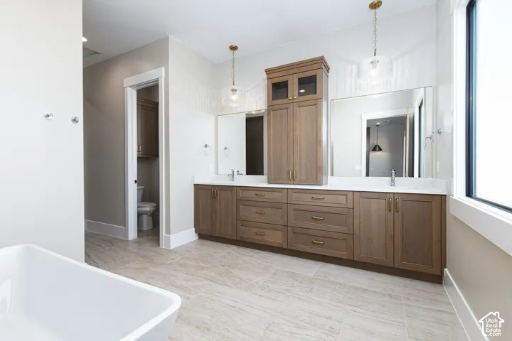Spa-inspired primary bathroom featuring an expansive wood-finish vanity with dual sinks, abundant storage cabinetry, and polished countertops