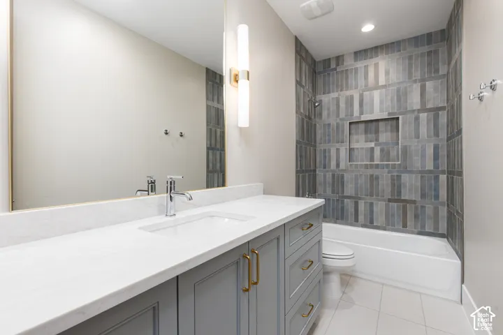 Vanity with a white countertop and undermount sink, brass-finished hardware, a large wall-mounted mirror, and a tiled shower-tub combination with a built-in niche