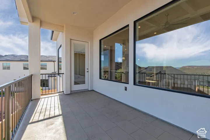 Covered balcony with tile flooring, featuring a glass-paneled door and large windows with black trim